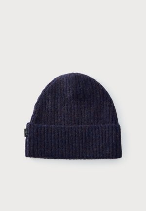 Bonnet en tricot côtelé bleu marine foncé avec revers plié et petite étiquette noire sur le côté, présenté sur un fond clair uni.