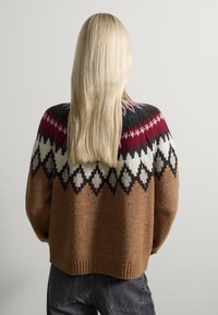Pull en laine marron avec un motif géométrique en blocs de couleurs bleu marine, rouge et crème. Bas à côtes et texture douce.