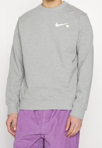 Grå sweatshirt i bomullsblandning med rund halsringning, långa ärmar, ribbade muddarna och en vit Nike-logotyp med en gul hjärtDetalj.