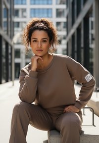 Brązowa, teksturowana bluza dresowa z dopasowanymi spodniami. Posiada okrągły dekolt, ściągacze na rękawach oraz naszywkę na lewym rękawie z napisem.