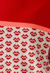 Strickpullover mit einem roten oberen Abschnitt und einem cremefarbenen unteren Abschnitt, der ein sich wiederholendes rotes Lippenmuster aufweist; beinhaltet ein pinkes Akzentband.