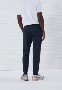 Mörkblå träningsbyxor med elastisk midja och smalnade anklar, kombinerat med en enkel vit T-shirt och silverfärgade träningsskor.