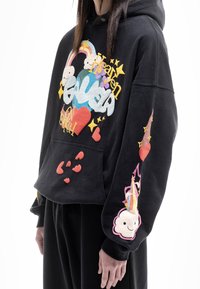 Sudadera negra con estampados gráficos coloridos, que incluyen nubes, estrellas y corazones. Presenta un bolsillo delantero y mangas con puños. Textura suave.