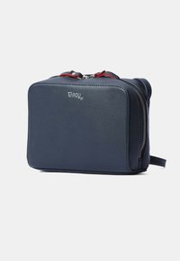 Borsa in pelle blu navy di forma rettangolare, con cerniere, dettagli rossi e logo sul davanti. Texture liscia con un design compatto.