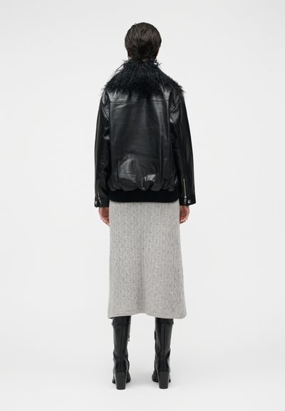 Μαύρο δερμάτινο μπουφάν με χνουδωτό γιακά, γκρι πλεκτή φούστα με ριμπ ύφανση και μαύρες μπότες μέχρι το γόνατο. Η εμφάνιση χαρακτηρίζεται από εφαρμοστή, σύγχρονη σχεδίαση.