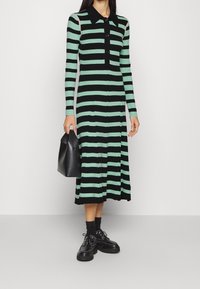 Abito lavorato a maglia con righe verticali nere e verde menta, maniche lunghe, colletto nero e frontale con bottoni. Abbinato a una borsa nera.