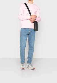 Felpa rosa in cotone con scollo tondo, jeans in denim azzurro chiaro e sneakers grigie con dettagli rossi. Borsa a tracolla nera indossata a tracolla.