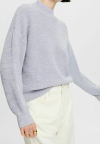 Lichtpaarse gebreide trui met een col en verlaagde schouders; gecombineerd met gebroken witte broek. Heeft een losse pasvorm en geribbelde boorden.