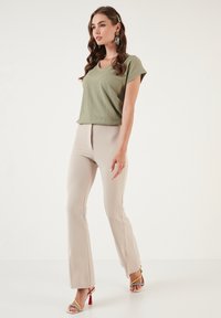 Olive green short-sleeve top with a ribbed texture, paired with beige flared pants. Accessories include colorful heeled sandals and earrings.