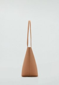 Tapered tan handtas met een lange enkele schouderband, gemaakt van glad materiaal, met een minimalistisch ontwerp en naadloze zijkanten.