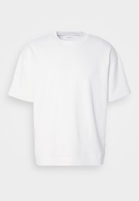 Sweat-shirt blanc oversize à manches courtes avec encolure ronde, coutures visibles et une petite étiquette sur la couture latérale.