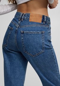 Modré džíny s vysokým pasem z denimu s koženou štítkem vzadu, klasickým designem s pěti kapsami a oranžovými švy.