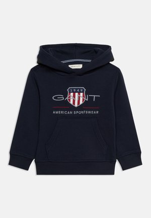 Tengerészkék kapucnis pulóver elülső zsebbel, „GANT" logóval, pajzs emblémával és „1949" felirattal, valamint „American Sportswear" szöveggel a mellrészen.