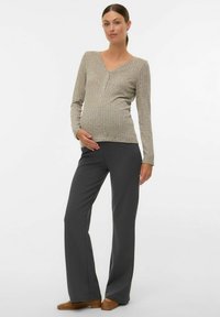 Bežīgs, garām piedurknēm ar rievotu rakstu, V veida izgriezumu un pogām, kopā ar tumši pelēkām, plašām biksēm un brūnām slip-on kurpēm.