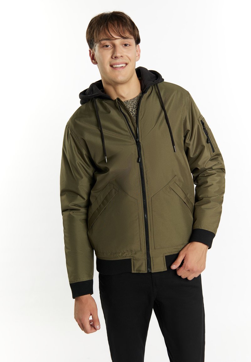 Giacca bomber verde oliva con cappuccio nero, chiusura con zip, tasche laterali e polsini a costine. Tessuto liscio, materiale resistente e design minimalista.
