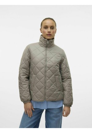 Veste matelassée gris clair avec un col montant, fermeture éclair sur le devant et manches longues, portée par-dessus une chemise rayée bleue et blanche.