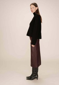 Pull en maille côtelée noir à col roulé, associé à une jupe midi en cuir bordeaux et des bottes noires à talons aiguilles. Texture lisse, silhouette structurée.