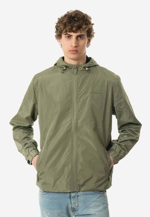 Giacca leggera verde oliva con cappuccio, zip frontale, polsini elastici e branding discreto sul petto. Tessuto liscio e resistente all'acqua.