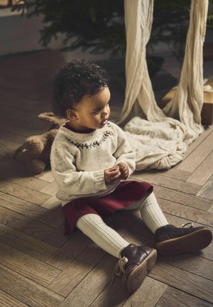 Strikket creme sweater med farverig broderi, parret med en kastanjebrun nederdel og creme ribbede strømpebukser. Brune lædersko med snørebånd.