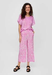 Blouse à motif floral rose avec encolure froncée, associée à un pantalon large assorti. Portée avec des sandales noires à lanières.