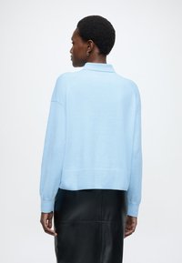 Lichtblauwe gebreide trui met kraag, voorzien van geribbelde manchetten en zoom, gedragen over een zwarte leren rok. Soepele textuur met een losse pasvorm.