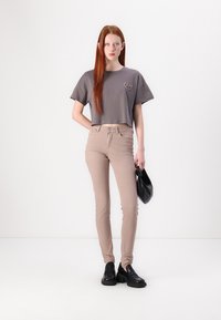Gray cropped t-shirt with logo, beige skinny pants, black shoes, and a black handbag, set against a light background.