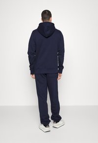 Conjunto de sudadera y pantalones deportivos en color marino, hecho de una tela suave. La sudadera cuenta con un cordón y un bolsillo tipo canguro. Los pantalones deportivos tienen un bolsillo lateral y puños acanalados.