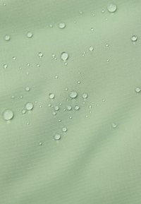 Tessuto verde chiaro con una superficie texture, caratterizzato da molteplici gocce d'acqua su di esso, che evidenziano le sue proprietà impermeabili.