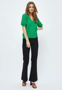 Pull en tricot vert avec un col en V et des manches bouffantes ; associé à un pantalon noir évasé et des sandales à talons marron. Texture lisse et design décontracté.