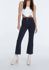 Höga midje, mörk denim flare-byxor med dragkedjeförslutning fram och sömmar, kombinerat med en off-white crop top och beige plattformstövlar.