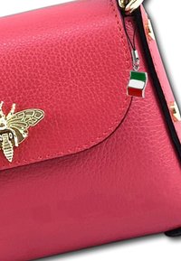 Roze leren handtas met een gestructureerde afwerking, voorzien van een gouden bij-embleem en een charm met de Italiaanse vlag, bevestigt aan de schouderband.