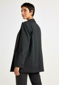 Stribet sort blazer med brede revers, enkeltknap foran og to sidelommer. Skræddersyet pasform med en let oversized form.