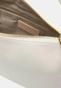 Interno di una borsa in pelle bianca con fodera beige, zip dorata e un'etichetta con la scritta "Coccinelle, Pelle Italiana Autentica."