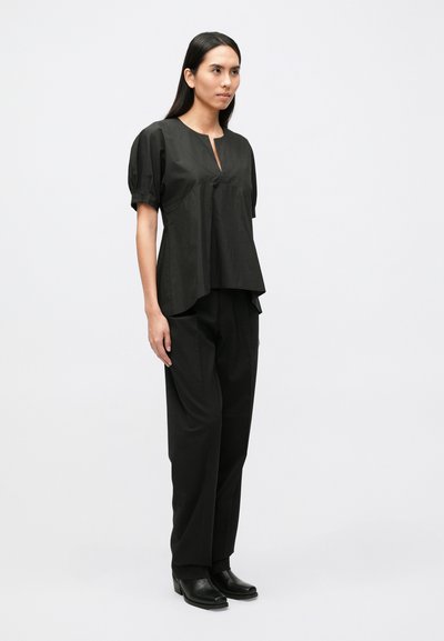 Fekete pamut rövid ujjú felső kulcslyuk nyakkivágással, fekete nadrággal párosítva. Simas textúra és laza szabás, rétegezett hatást keltve.