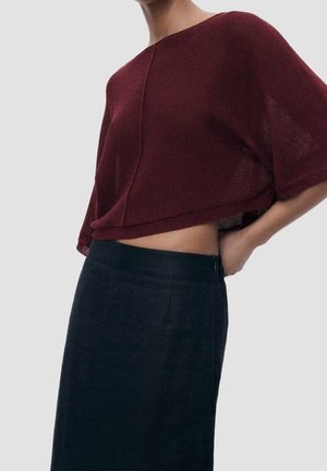 Bourgognefarvet cropped sweater med korte ærmer og tekstureret strik. Kombineret med en sort højtaljet nederdel, der viser en elegant silhuet.