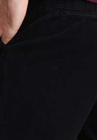 Pantaloni negri din bumbac cu o textură netedă, dotată cu buzunare laterale și o croială clasică. Designul include un buzunar discret la spate.