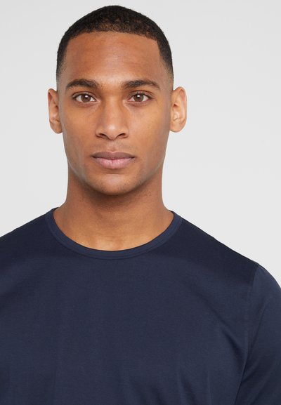T-shirt bleu marine à manches courtes avec un col rond, fabriqué en tissu lisse. Gros plan sur le haut du corps et le visage d'un modèle masculin.