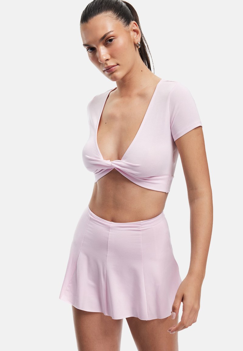 Lyserød crop top med dyb V-udskæring og knudedetalje, der er parret med en matchende udvidet mini-nederdel. Glat, strækbart stof.