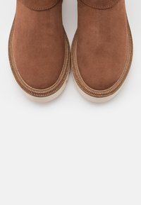 Brązowe zamszowe botki za kostkę o zaokrąglonym nosku, z fakturowanymi bokami i jasną gumową podeszwą z ozdobnym żebrowanym brzegiem.