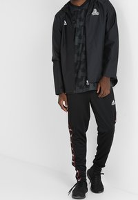 Czarny sportowy strój z kurtką na zamek i wzorzystą koszulką, do kompletu spodnie z czerwonymi akcentami o dopasowanym kroju.