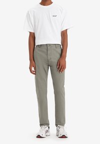 Biała koszulka z krótkim rękawem z czarnym logo „Levi's”, zestawiona z jasnooliwkowymi spodniami i białymi tenisówkami z czerwonymi akcentami.