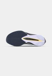 Semelle de chaussure de sport noire et blanche avec un motif en caoutchouc texturé, accent jaune et une semelle intermédiaire blanche lisse comportant des détails de marque et de design.