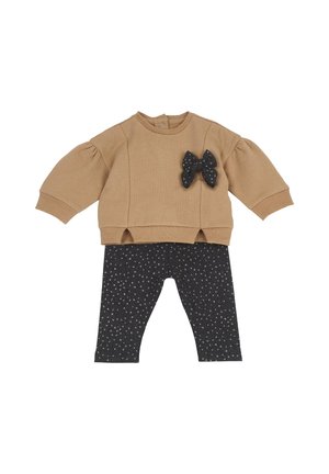 Maglietta beige a maniche lunghe per neonati con dettaglio fiocco nero abbinata a leggings neri con piccoli motivi floreali bianchi.