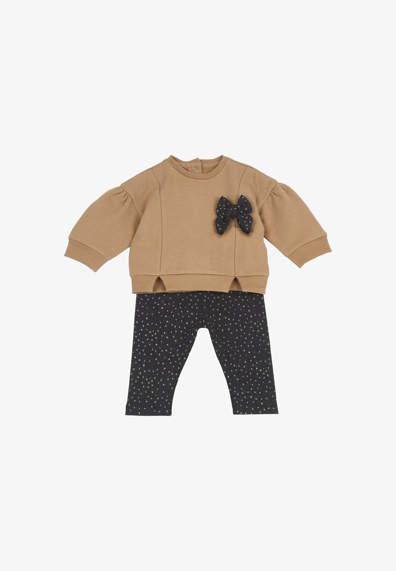 Haut bébé beige à manches longues avec un détail nœud noir, associé à des leggings noirs avec de petits motifs floraux blancs.