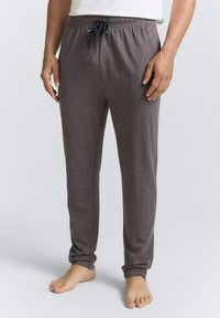 Pantalons de pyjama gris en tissu doux. Taille élastique avec un cordon de serrage navy. Design de jambe fuselée, portés pieds nus.