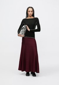 Bluză neagră cu mâneci lungi și margine albă ondulată, asortată cu o fustă lungă burgundă. Ține un plic gri cu model de șarpe.