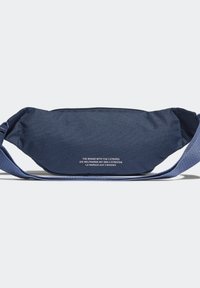 Tyrkysová látková ledvinka s uzávěrem na zip, nastavitelným popruhem a bílým textem na přední straně. Hladká textura a zakřivený tvar.