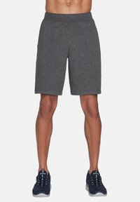 Bermudas atléticas grises hechas de una tela suave, con una cintura elástica y un corte holgado. Combinadas con zapatillas atléticas de color azul oscuro.