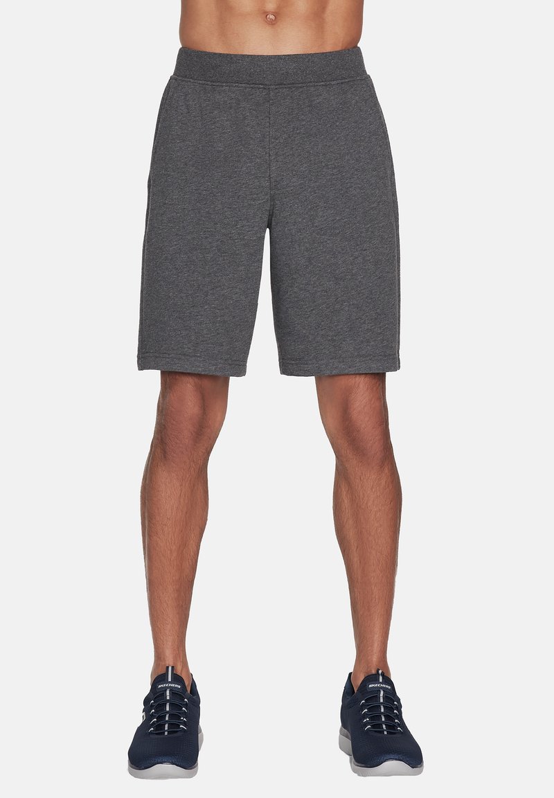 Bermudas atléticas grises hechas de una tela suave, con una cintura elástica y un corte holgado. Combinadas con zapatillas atléticas de color azul oscuro.
