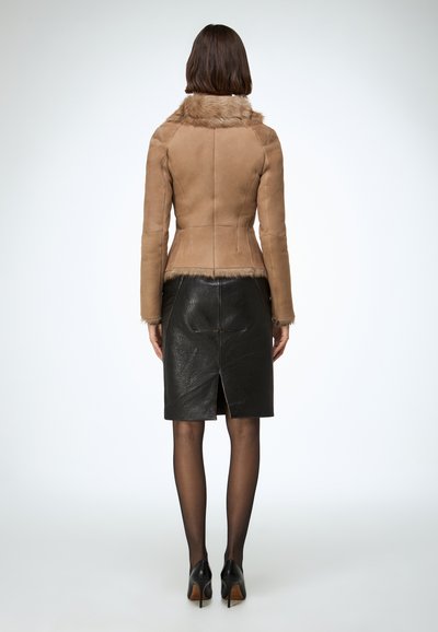 Veste en suède marron clair avec col en fausse fourrure, coupe ajustée et détails avec coutures au dos, associée à une jupe crayon en cuir noir.